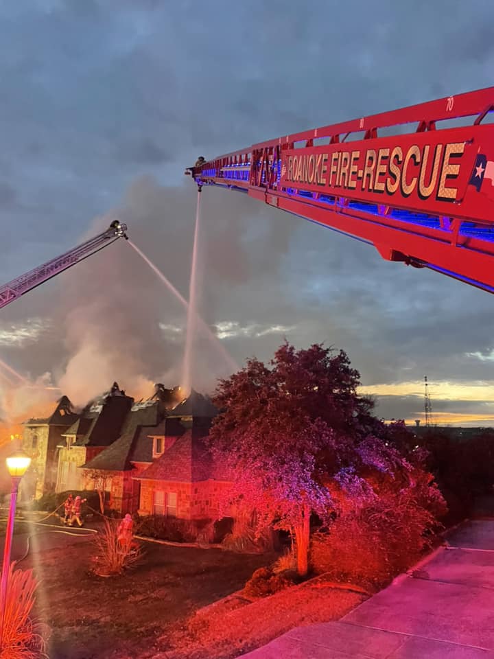 2 fire trucks putting water on a house that is on fire