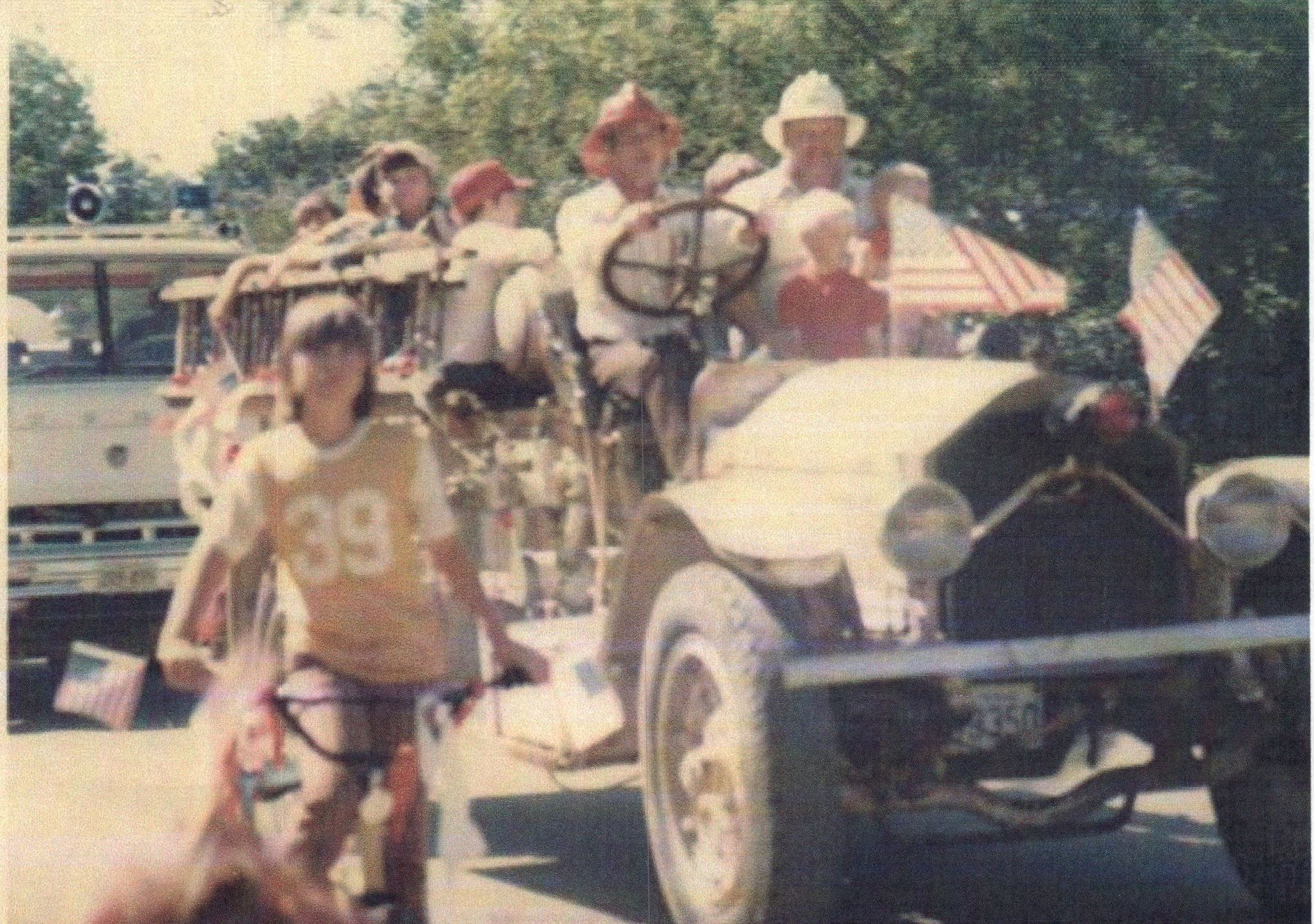 1923 fire engine in parade with men carrying American flags and driving the engine down the road 