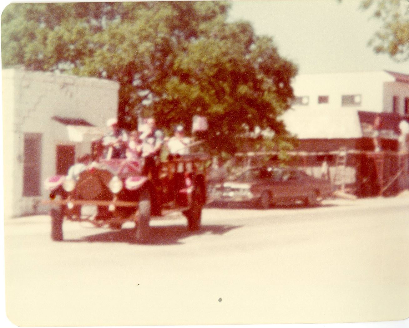 1923 fire engine in parade turning corner carrying people and flanked with American Flags on engine 