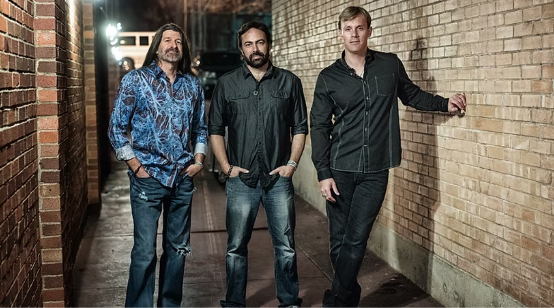 Three standing outdoors next to a brick wall.